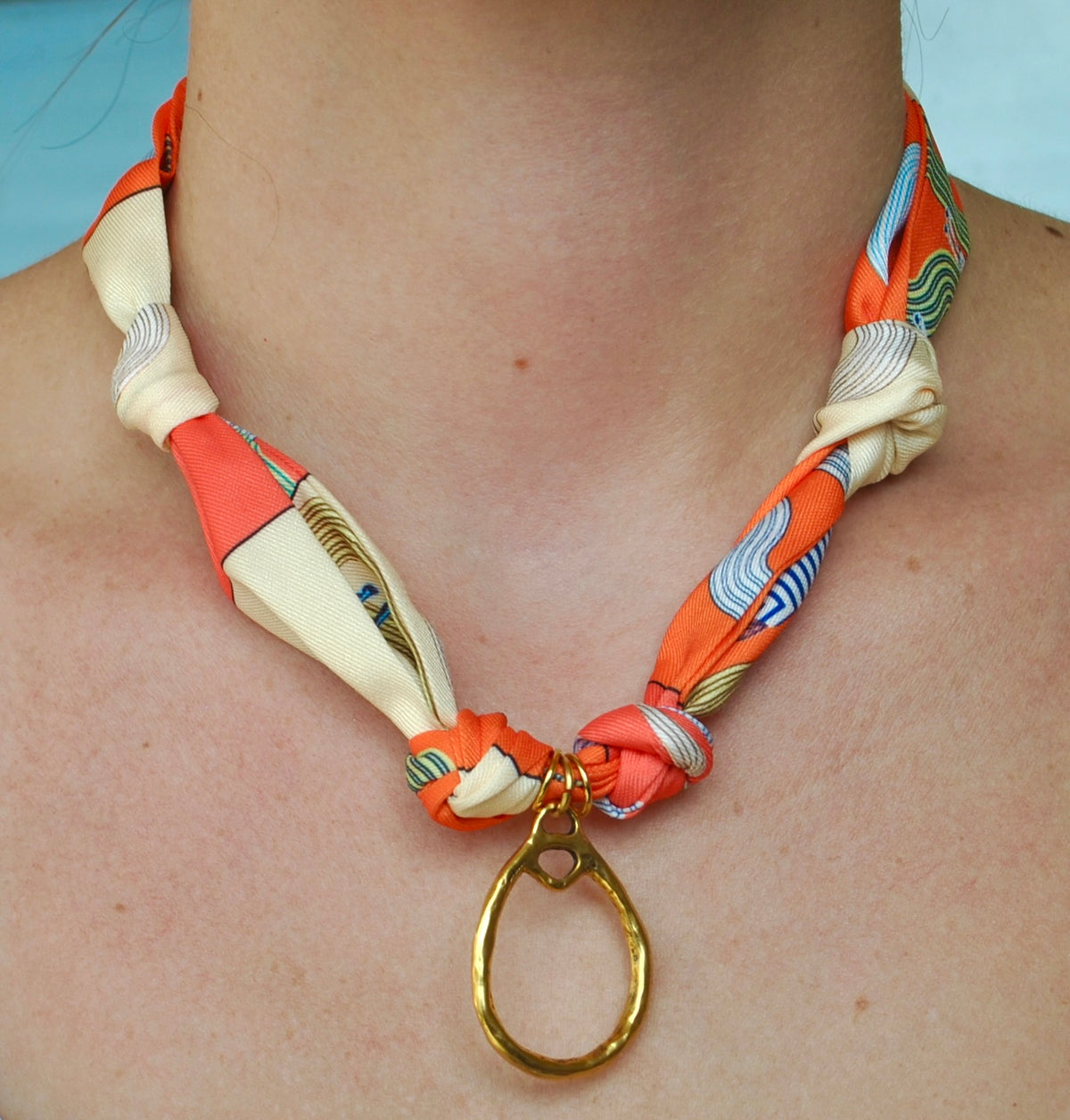 Coral cream and blue printed silk scarf necklace with large open gold teardrop pendant worn around neck