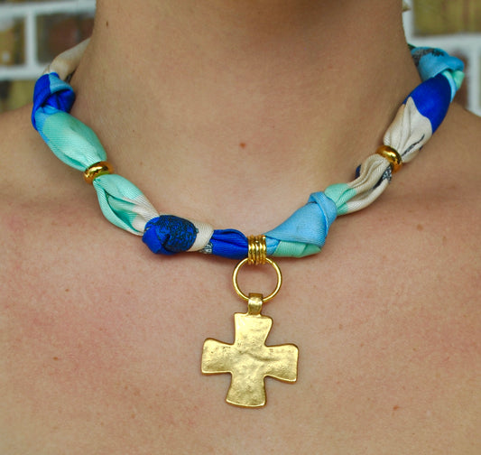 Blue twisted silk scarf necklace with gold cross pendant worn around neck