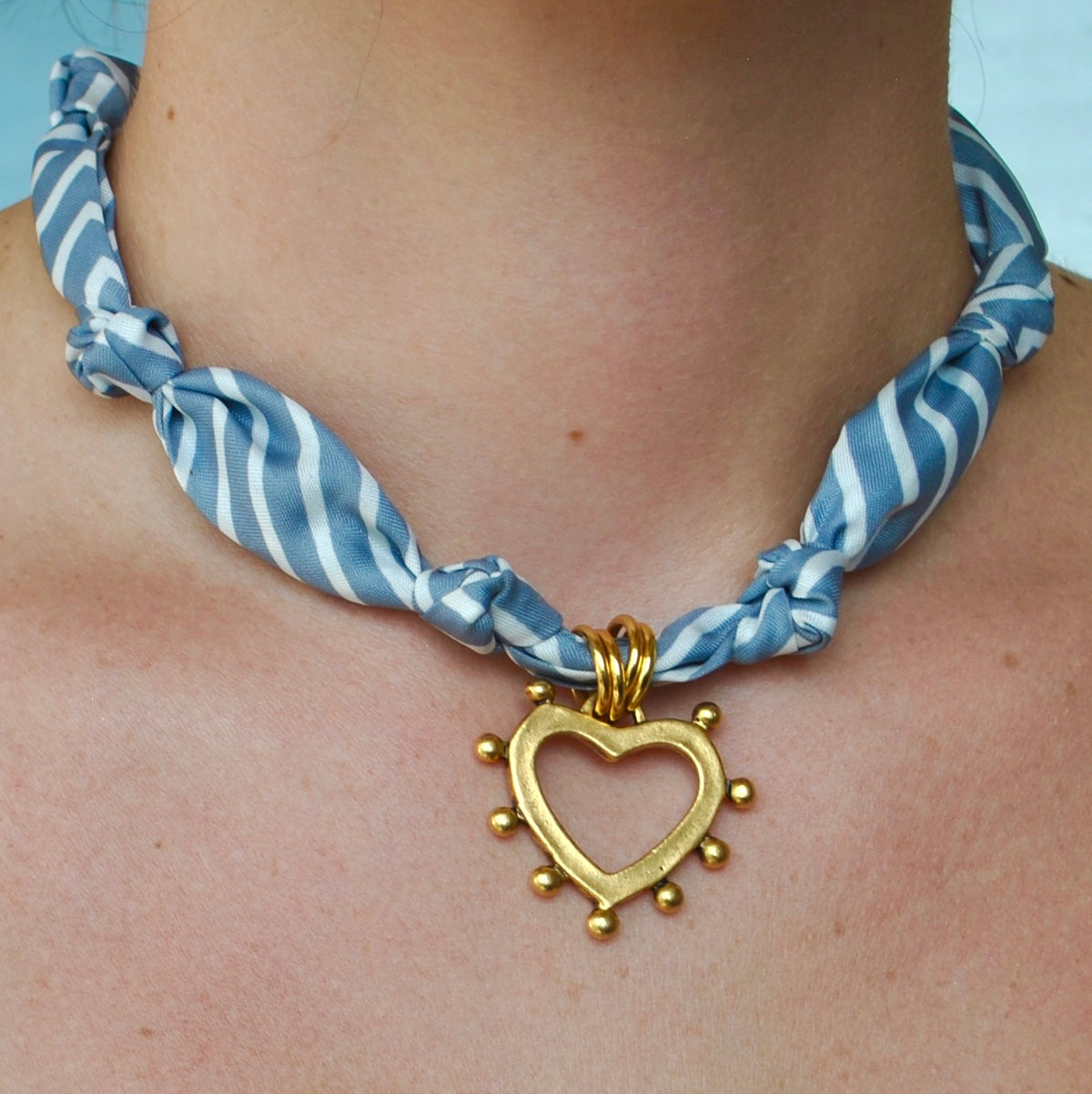 Blue and white stripe silk scarf necklace with open gold heart pendant worn around neck