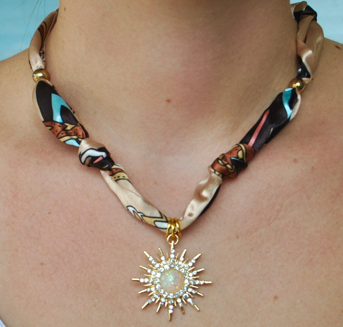 Taupe multicolor printed silk scarf necklace with large crystal sunburst and opal pendant worn around neck