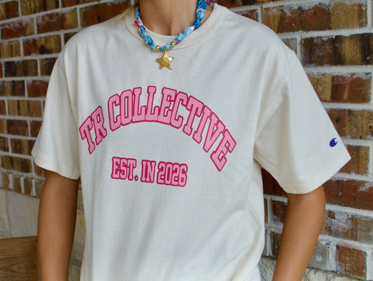 Cream TR Collective short-sleeve tee with pink varsity-style lettering and a Champion sleeve logo